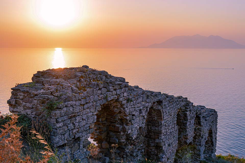 The remains of a stone arch perched on the edge of a cliff overlooking a sea